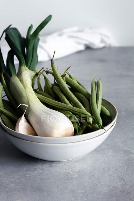 Tigela branca com alho e cebola verde e feijão verde na mesa na cozinha — Fotografia de Stock