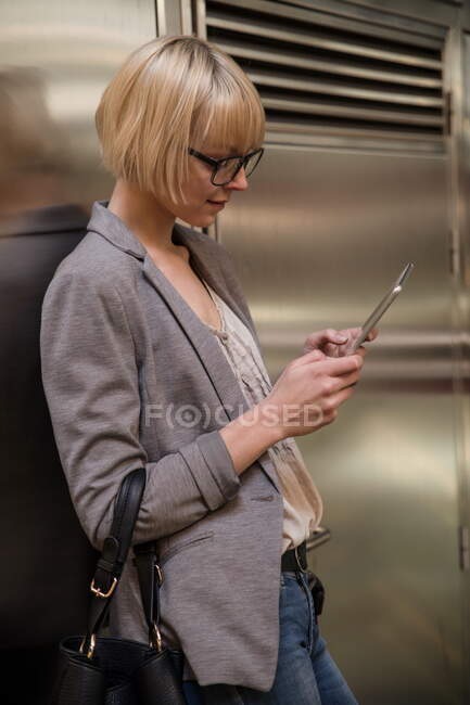 Seitenansicht einer blonden Geschäftsfrau, die sich an eine Metallwand lehnt und auf einem Tablet surft — Stockfoto