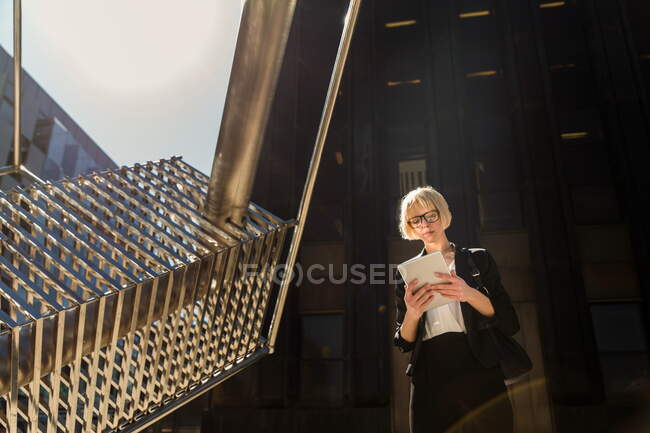 Стильна приваблива бізнес-леді стоїть і переглядає цифровий планшет на вулиці — стокове фото