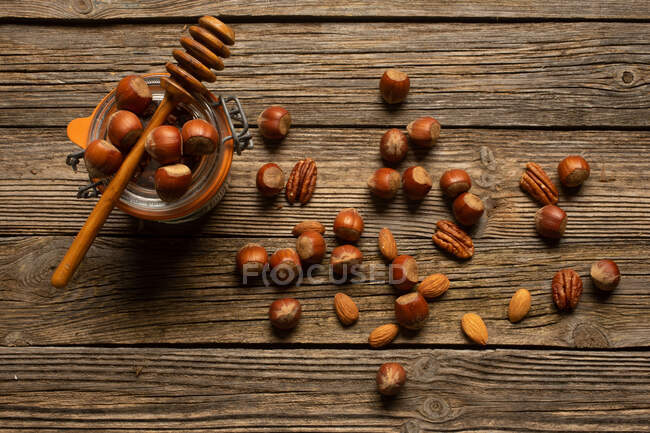 Vista dall'alto di nocciola con noce pecan e mandorla vicino vaso e tuffatore di miele in legno sul tavolo — Foto stock