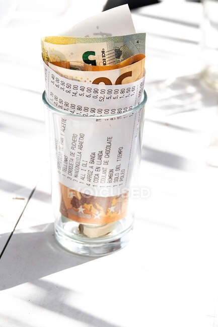 De cima do dinheiro de papel enrolado com conta no vidro na mesa abaixo do sol brilhante — Fotografia de Stock