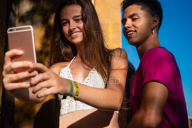 Charming young lady taking selfie on phone with content ethnic guy — Stock Photo