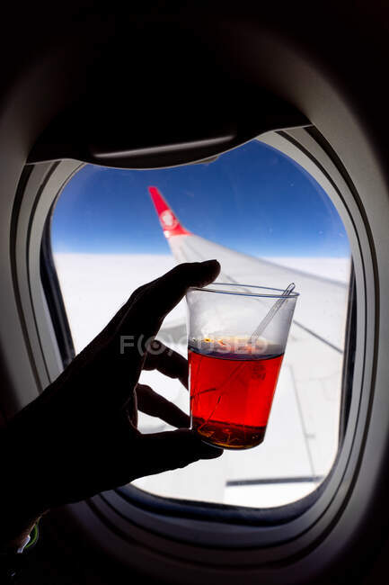 Passageiro sem rosto com xícara de chá de plástico durante o voo em avião no dia ensolarado — Fotografia de Stock