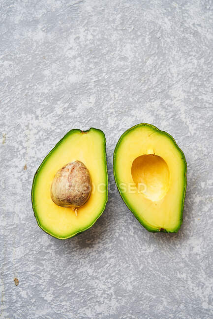 Top view of fresh ripe avocado cut in half on light grey texture background — Stock Photo