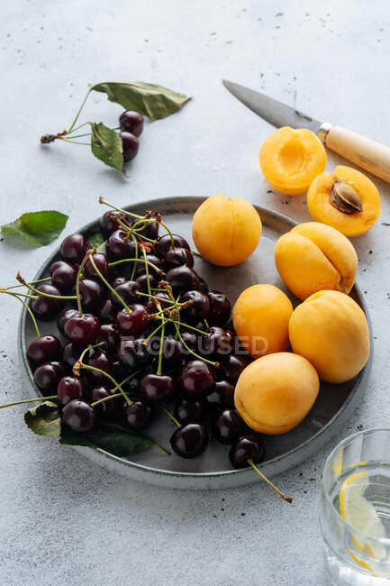 Flat lay of delicious cherry and yellow peaches served on plate on a white background. — Stock Photo