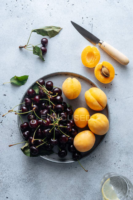 На білому тлі на тарілці подають смачну вишню та жовті персики.. — стокове фото