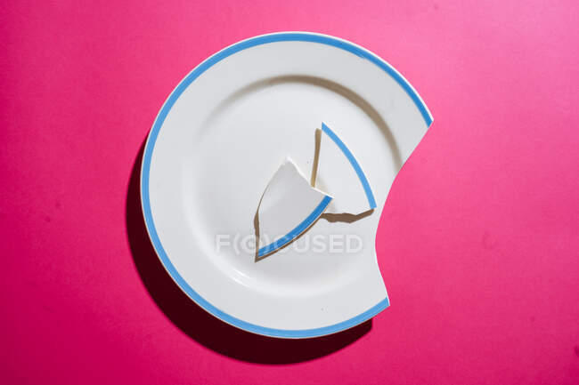 Разбитая белая тарелка на розовом фоне — стоковое фото