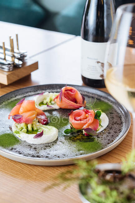 Salmon rolls with onion and herbs served on metal plate on wooden table with glass and bottle of white wine — Stock Photo