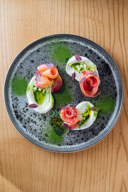 Rollos de salmón con cebolla y hierbas servidas en plato rústico sobre mesa de madera - foto de stock