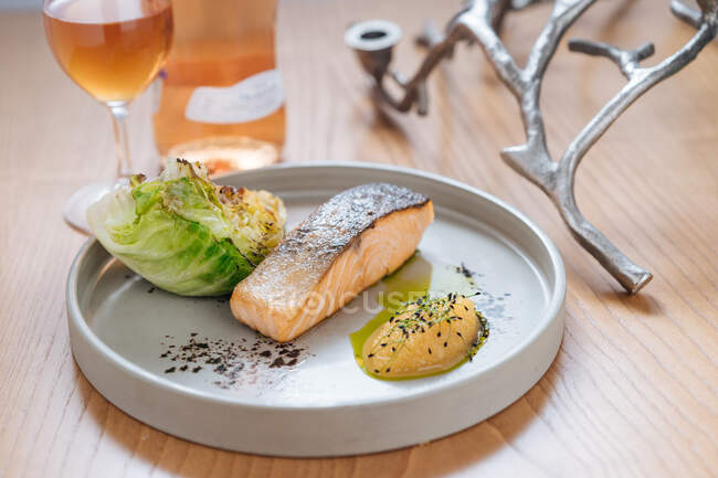 Steamed salmon served with grilled cabbage on white ceramic plate on wooden table with glass and bottle of wine — Stock Photo