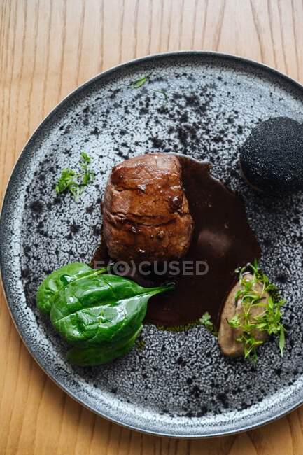 Vista dall'alto di deliziosa bistecca di carne gourmet con salsa ed erbe servite su piatto d'argento in metallo su sfondo di legno — Foto stock