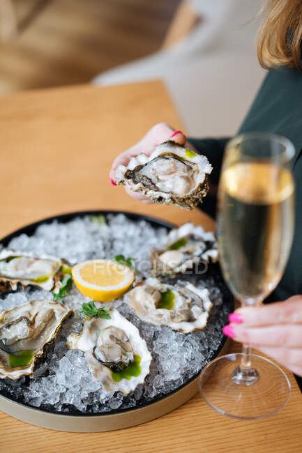 Unrecognizable cropped person with glasses of champagne trying delicious oysters with lemon and herbs in restaurant — Stock Photo