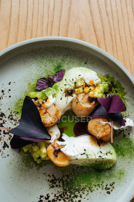 Gedämpfte weiße Fischsteaks mit Garnelen und lila Basilikumblättern auf weißem Teller garniert mit grünem Matcha-Pulver auf Holztisch — Stockfoto