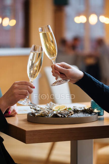 Unrecognizable couple with glasses of champagne trying delicious oysters with lemon and herbs in restaurant — Stock Photo