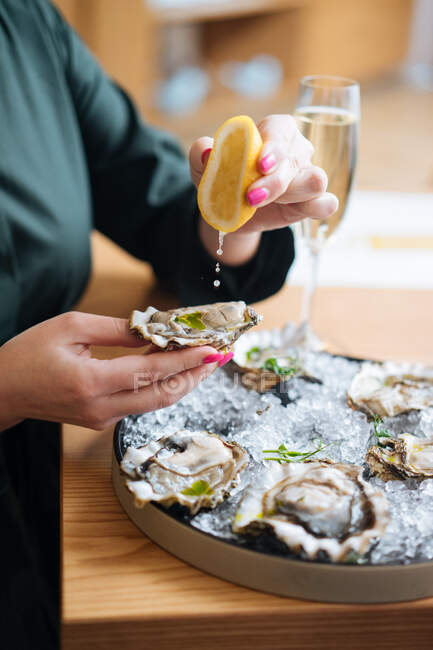 Personne coupée méconnaissable avec des verres de champagne en essayant de délicieuses huîtres au citron et aux herbes au restaurant — Photo de stock