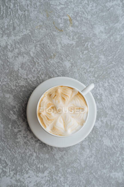 Vista superior da xícara de cappuccino quente com arte latte servida em disco branco em fundo texturizado cinza claro — Fotografia de Stock