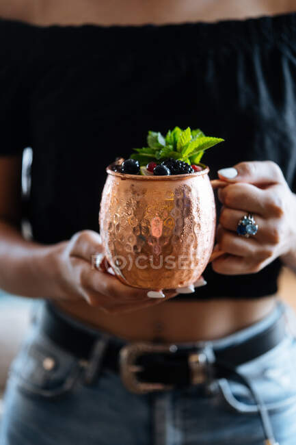 Неузнаваемая женщина несет металлическую кружку натурального фруктового напитка с ягодами и мятными листьями в летний день в кафе — стоковое фото