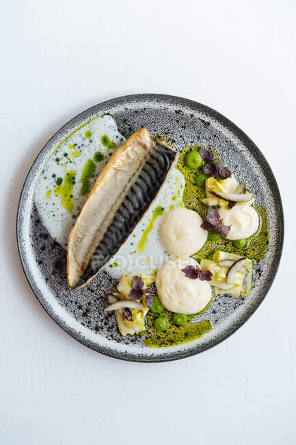 Dall'alto pezzo di pesce arrosto con salsa di crema gustosa ed erbe fresche poste sul piatto su sfondo bianco — Foto stock