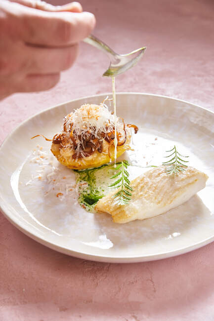 Persona irreconocible con cuchara añadiendo salsa crema a delicioso plato de pescado con hierba en el restaurante - foto de stock