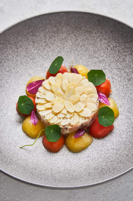 С высоты восхитительный рыбный тартар подается с миндалем и свежими помидорами черри на тарелке в ресторане — стоковое фото