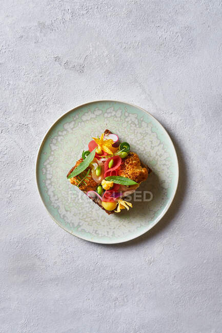 Von oben Ansicht leckeres Sandwich mit geschnittenem Gemüse und Blumen dekoriert und auf Teller auf weißem Tisch im Café platziert — Stockfoto