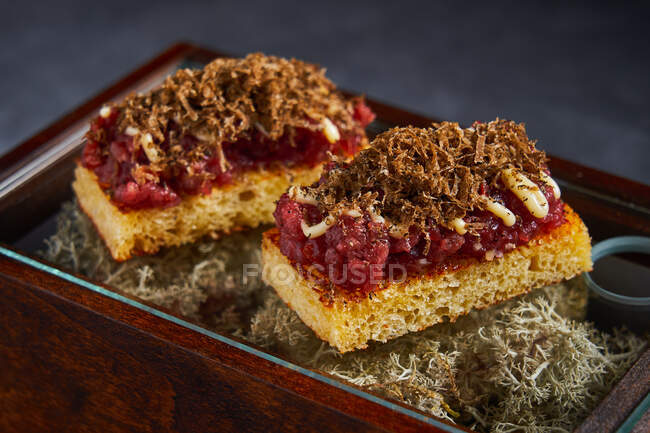 Pastel de esponja dulce con mermelada de bayas y rizos de chocolate colocados en caja con musgo seco - foto de stock