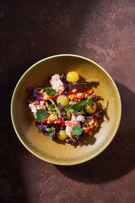 Vista superior da tigela com deliciosa salada de caranguejo com legumes frescos e ervas colocadas na mesa marrom — Fotografia de Stock