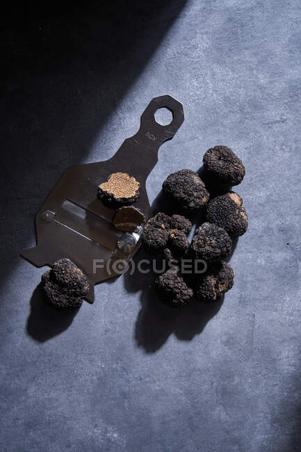 Зверху купа дорогих чорних трюфелів, розташованих біля металевої бритви на сірій поверхні штукатурки — стокове фото