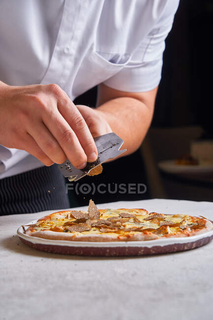 Unrecognizable cook slicing fresh truffle on tasty pizza while working in restaurant — Stock Photo