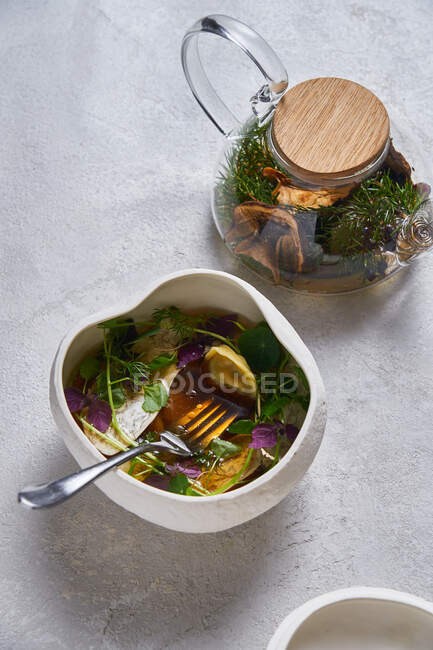 Fresh warm tea from glass teapot into ceramic bowl with herbs — Stock Photo