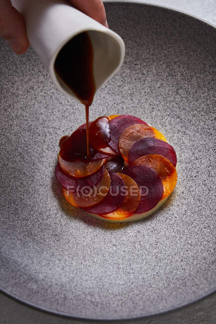 From above anonymous person adding sauce to delectable dish made of thin slices of boiled carrot and beetroot on plate — Stock Photo
