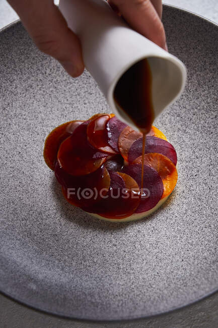 Da suddetta persona anonima che aggiunge la salsa a piatto delizioso fatto di fette sottili di carota bollita e barbabietola su piatto — Foto stock