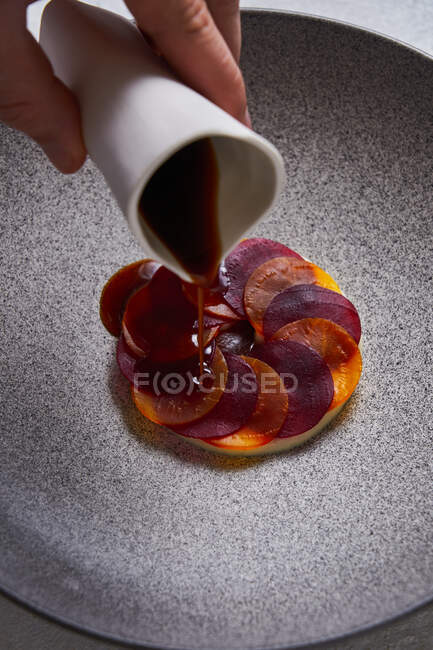 From above anonymous person adding sauce to delectable dish made of thin slices of boiled carrot and beetroot on plate — Stock Photo