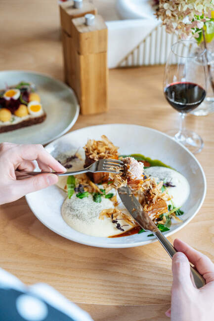 Geschnitten unkenntliche Person Hände essen Stücke von gebratenem Fleisch mit Trüffeln und frischen Kräutern auf dem Teller im Café serviert — Stockfoto