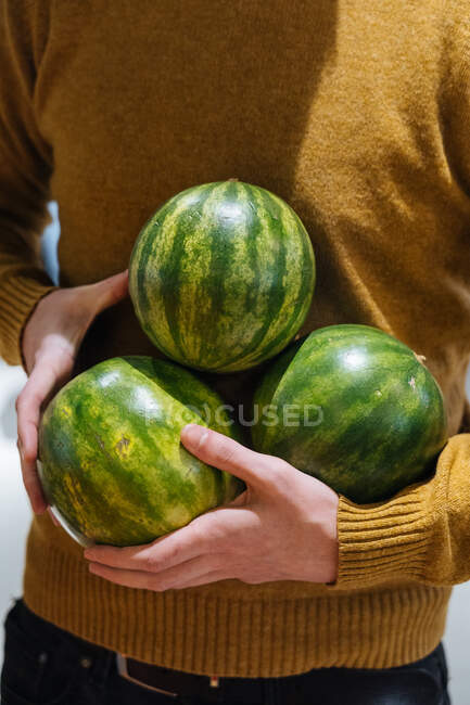Unrecognizable male carrying small ripe watermelons on sunny day on market — Stock Photo