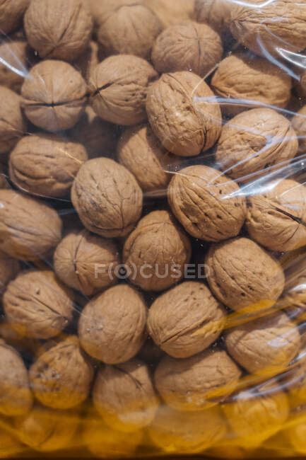 Primer manojo de nueces maduras colocadas dentro de una bolsa de plástico transparente en la tienda de comestibles - foto de stock