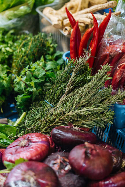 Hortelã fresca e alecrim colocados perto de cebolas vermelhas e pimentas em stall no mercado — Fotografia de Stock
