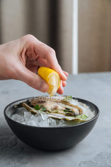 Pessoa cortada irreconhecível espremendo limão em deliciosas ostras no Ice cuber em uma tigela no restaurante — Fotografia de Stock