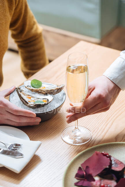 Personne coupée méconnaissable avec des verres de champagne en essayant de délicieuses huîtres au citron et aux herbes au restaurant — Photo de stock