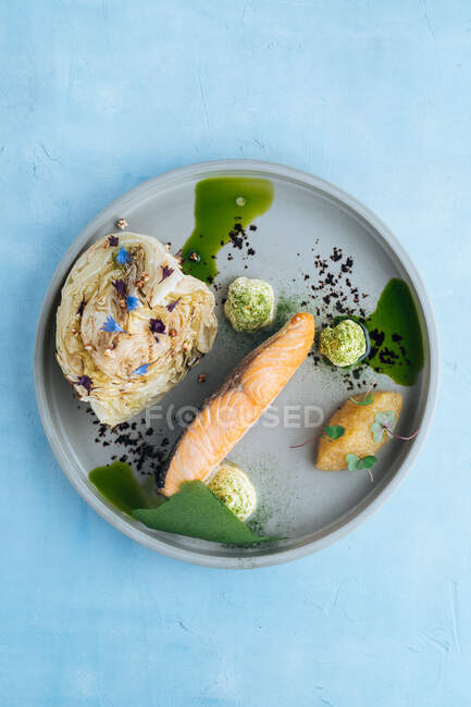 From above of baked salmon fillet and pike caviar with piece of young cabbage on stylish grey plate decorated with white sauce on blue background — Stock Photo