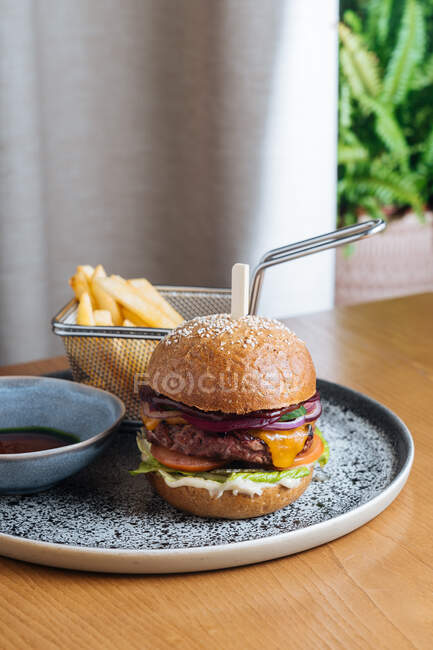 Appetitanregender Burger mit Wildpüree frisches Roggenbrot Brötchen rote Zwiebelkäsescheiben Tomaten Salatblatt und Sauce auf Teller mit Bratkartoffeln im Restaurant — Stockfoto