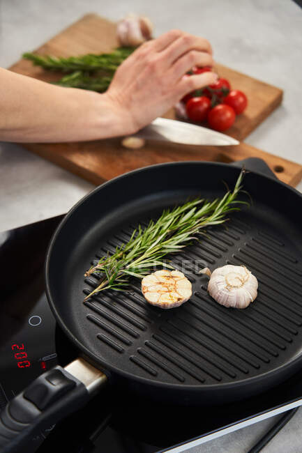 Grill pan with rosemary and garlic next to cooking woman — Stock Photo