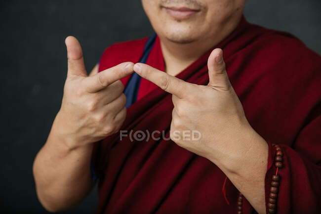 Primer plano de las manos de la cosecha rezando monje tibetano en túnica roja tradicional con gesto de manos simbólicas mudra - foto de stock