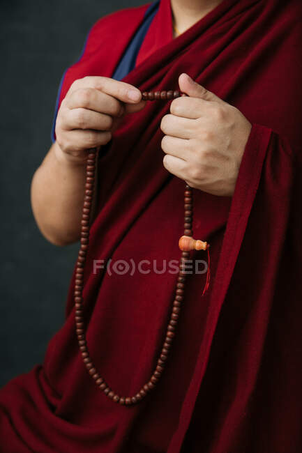 Vista lateral da colheita monge budista em roupas vermelhas tradicionais segurando contas de oração na mão — Fotografia de Stock