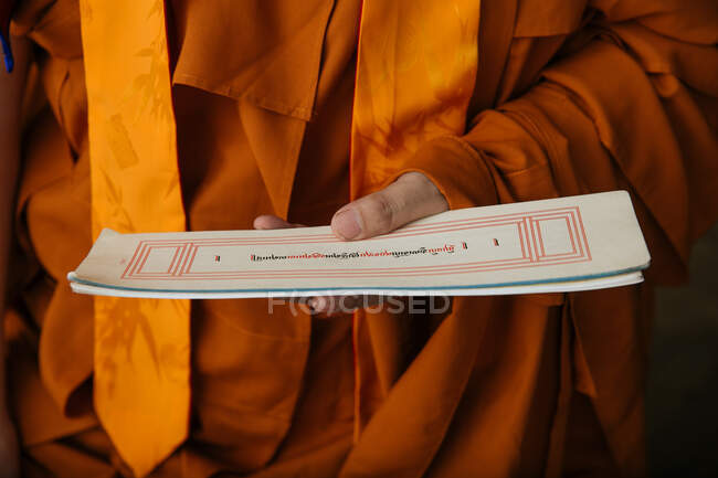 Cultivo monje budista tibetano en ropa naranja sosteniendo papel con texto ritual sagrado - foto de stock