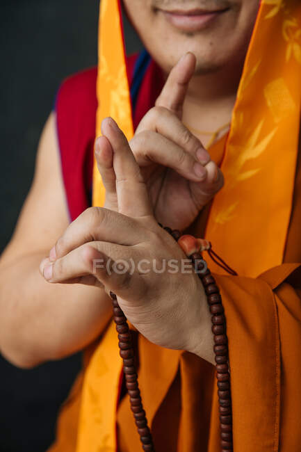 Crop Tibetan monk in traditional clothes with prayer beads doing mudra gesture with hands — Stock Photo