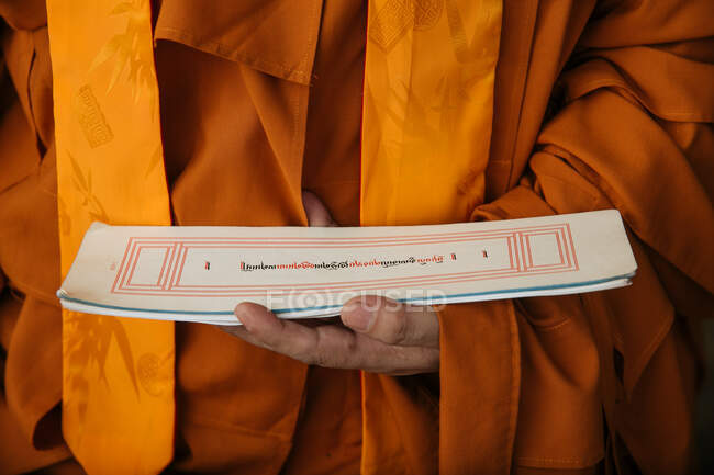 Crop Tibetan Buddhist monk in orange clothes holding paper with holy ritual text — Stock Photo