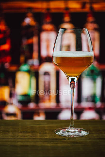 Beer in wineglass with foam in glass on wooden counter in bar on blur background — Stock Photo