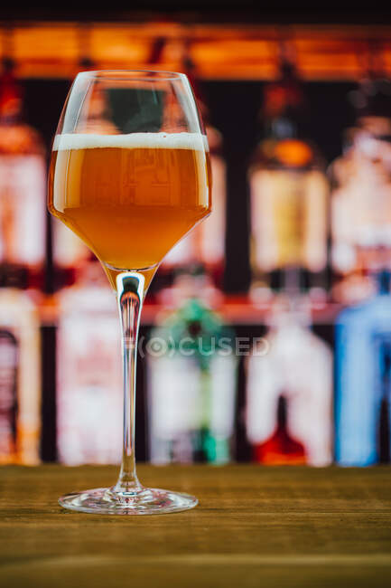 Cerveza en vino con espuma en vidrio sobre mostrador de madera en barra sobre fondo borroso - foto de stock
