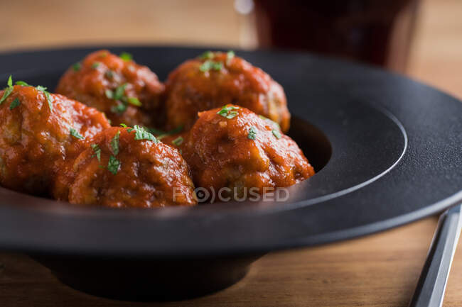 De arriba sabrosas albóndigas cocidas con salsa de tomate que sirven con pan en plato negro con cubiertos y bebidas en la mesa - foto de stock